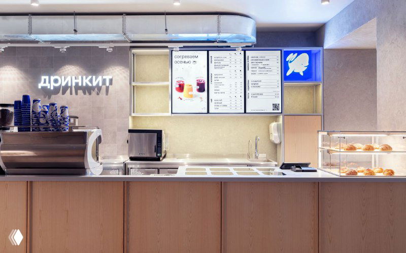 Фотография стойки кафе с меню и вывеской Drinkit: минималистичный интерьер, синие акценты в оформлении и логотип на световом коробе.