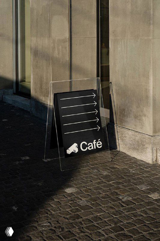 Уличный указатель‑«A‑frame» с чёрным фоном и стрелками навигации; демонстрирует применение фирменной графики и ориентиры для посетителей музея.