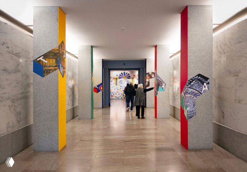 Внутренний холл музея: колонны и стены с графическими вставками и трёхмерным логотипом, показывающие интеграцию айдентики в навигацию и интерьерное оформление.