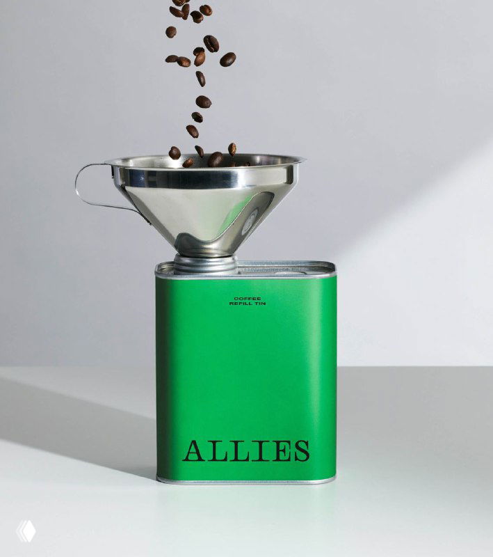 Зелёная металлическая банка с надписью ALLIES и воронкой сверху; падающие кофейные зёрна подчеркивают продуктовую съёмку на белом фоне с минималистичной подачей