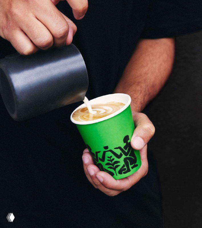 Бариста наливает молоко в чашку с зелёным бумажным стаканчиком ALLIES: кадр демонстрирует брендированный стрит-кофе и применение фирменной цветовой палитры