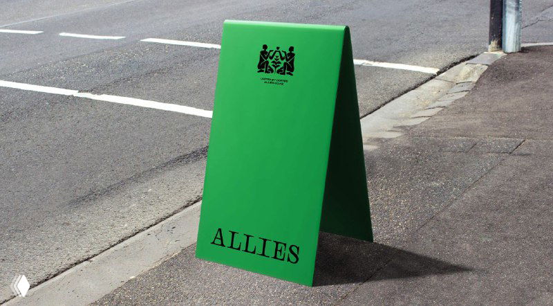 Зелёный уличный штендер с крупным логотипом ALLIES, установленный на тротуаре — пример наружной брендированной вывески в городской среде