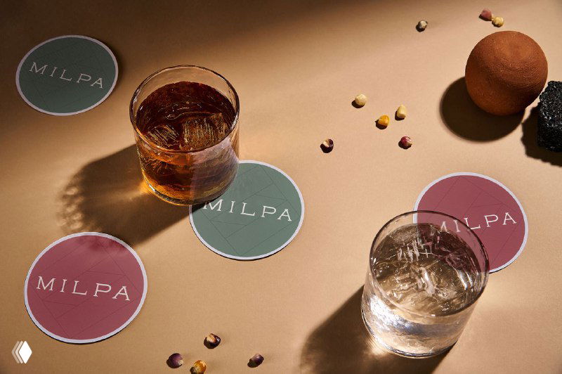 Коастеры с надписью MILPA и два низких стакана с напитком на бежевом фоне; студийная постановка с мягкими тенями и брендовым акцентом.