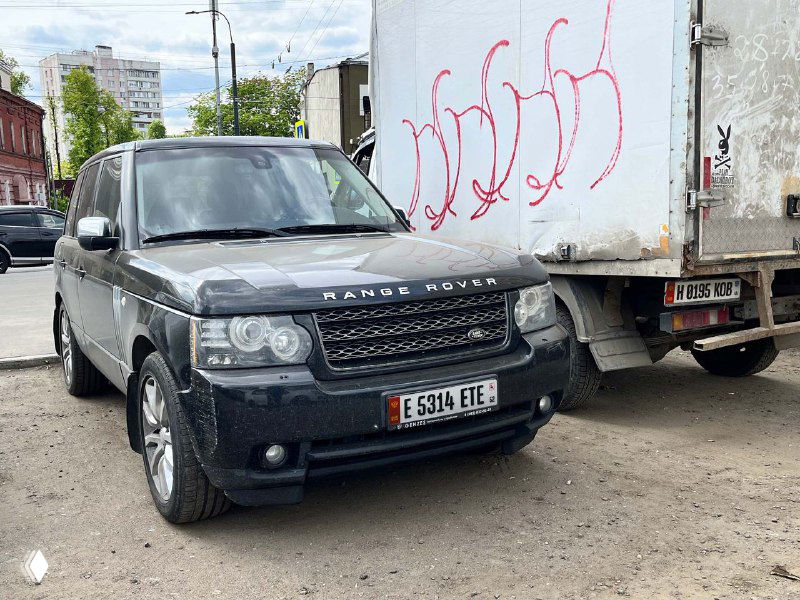 Внедорожник Range Rover на парковке с нестандартным регистрационным знаком в передней части, крупный план корпуса и соседних автомобилей.
