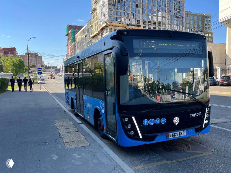 Городской автобус синего цвета с хорошо видимым вариантом номерного знака на передней панели, общий вид улицы и здания в отражении.