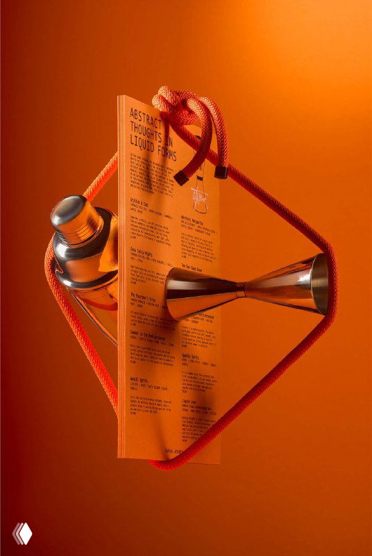 Меню и печатные листы Gaya Athens в динамичной композиции с верёвками и металлическим предметом на оранжевом фоне; кадр подчёркивает объём и конструкцию презентации.