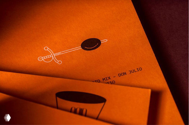 Деталь полиграфии Gaya Athens: минималистичная монохромная иконография и небольшая иллюстрация на оранжевой бумаге, демонстрирующая аккуратность реза и печати.