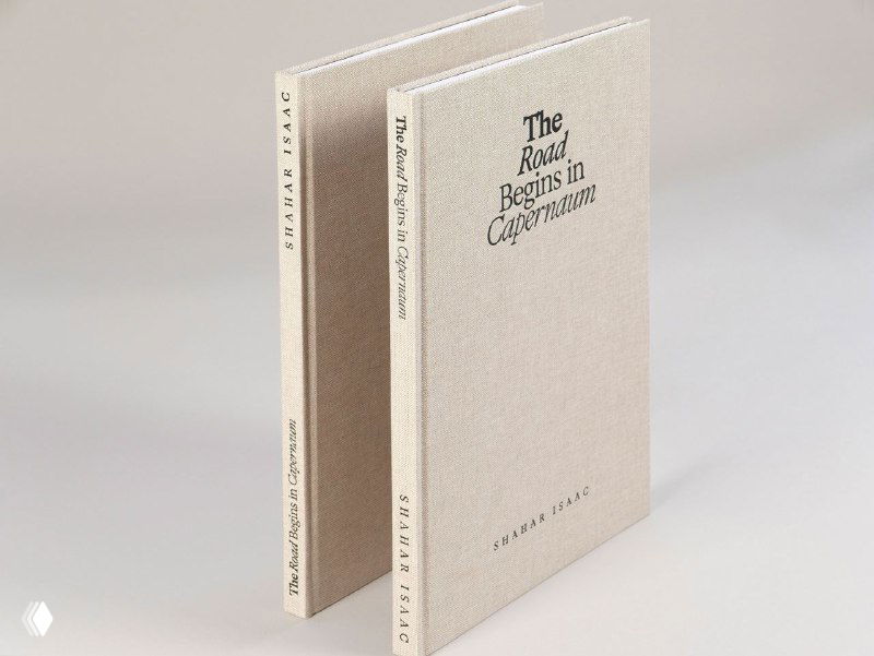 Две копии фотокниги «The Road Begins in Capernaum» в светлой тканевой обложке, показаны корешки и лицевые стороны на нейтральном фоне.
