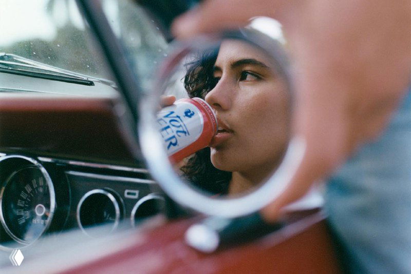 Кадр через боковое зеркало автомобиля: женщина пьёт из банки Not Beer, отражение и композиция подчёркивают фирменный стиль упаковки.