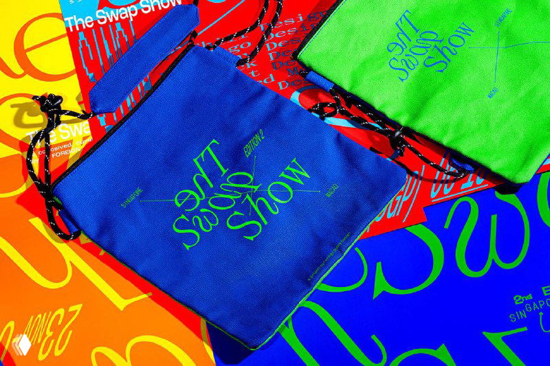 Крупный план ярких мешочков с логотипом The Swap Show на кислотном разноцветном фоне, насыщенные неоновые заливки.