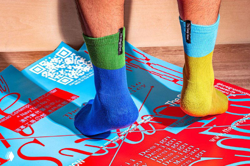 Ноги в разноцветных носках стоят на напечатанном постере с QR-кодом и крупной хаотичной типографикой The Swap Show, фрагмент кампании.