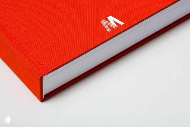 Крупный план красной тканевой обложки переиздания NYCTA Graphics Standards Manual — угол книги на белом фоне с фокусом на фактуру переплёта.