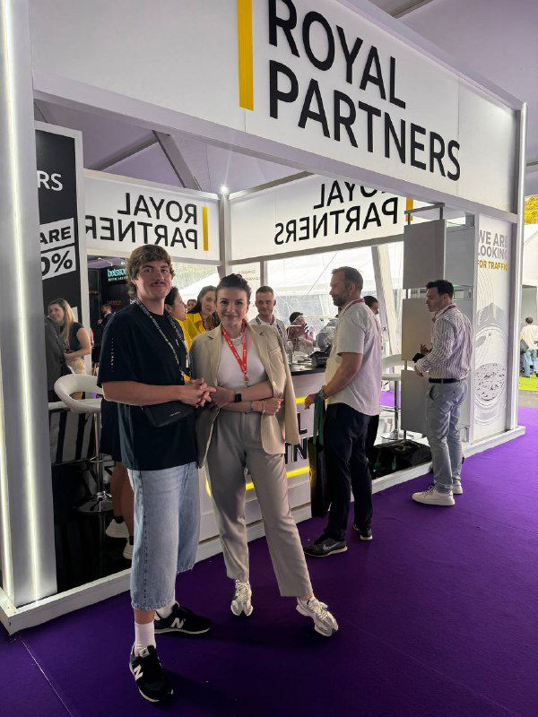 Group of Zillion Games staff and partners standing near the 'ROYAL PARTNERS' booth at SBC Summit in Lisbon, networking and chatting.