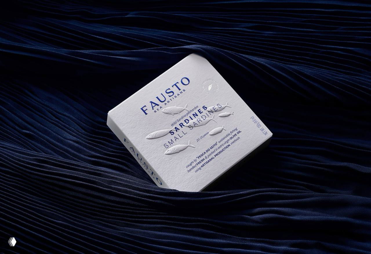Белая квадратная коробка с тиснением в виде рыб и синим логотипом FAUSTO на фактурном картоне, снятая на тёмной бархатной ткани для контраста.