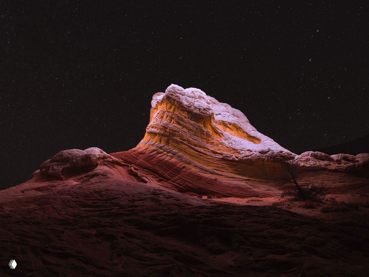 Пейзаж с освещённой горной формацией на фоне плотного звёздного неба; свет дрона выявляет слоистую структуру породы.