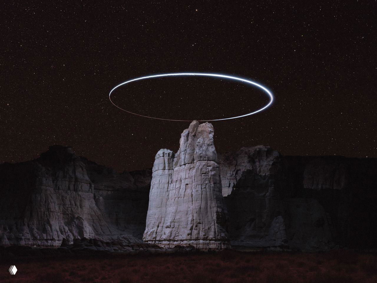 Ряд красных скал на переднем плане и тёмное небо; подсветка дрона выявляет текстуру, слоистость и форму рельефа.