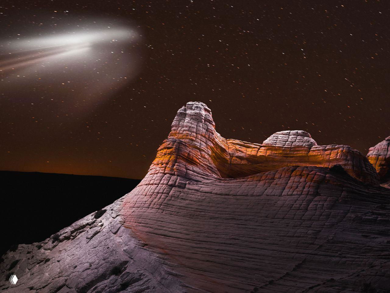 Группа скал с несколькими светящимися кольцами над ними; длинная выдержка фиксирует движение света и звёзд, создавая внеземной вид.