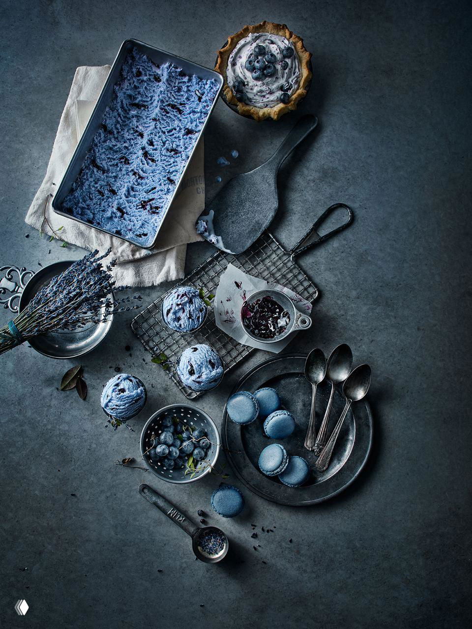 Холодная сине-фиолетовая фуд-фотография: голубые макароны, шарики мороженого и ягодные элементы на тёмном фоне в декоративной кулинарной компоновке.