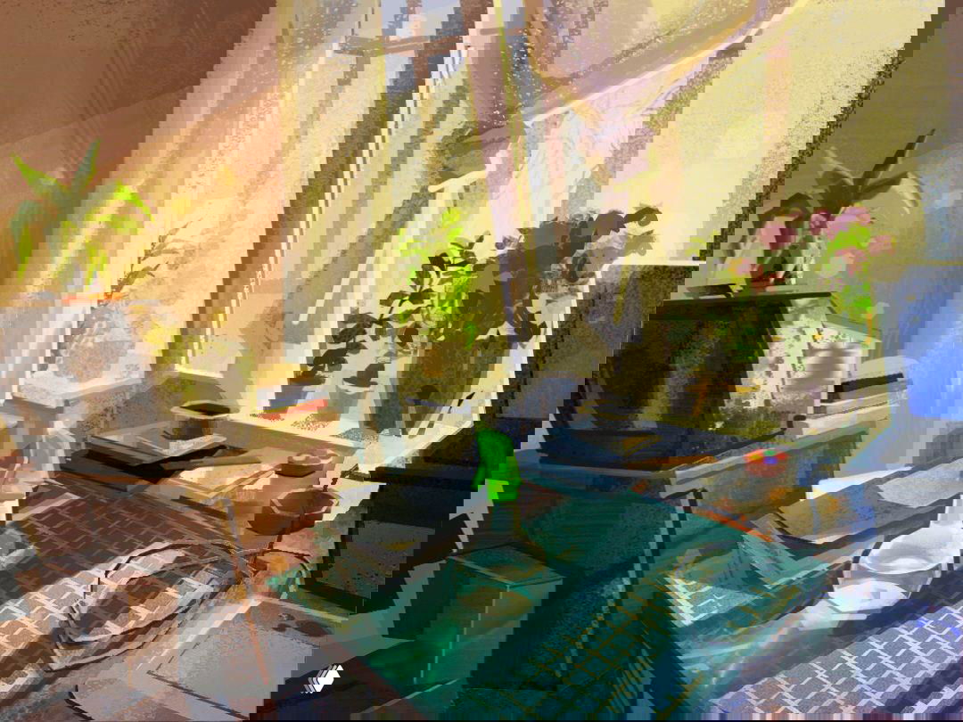 Рабочий стол художника у окна: разделочная карта, спрей-бутылка и растения на подоконнике в золотистом свете, атмосфера мастерской и творчества.