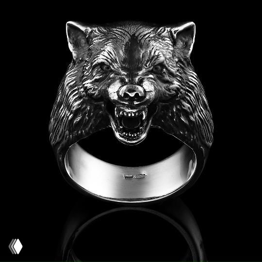 Крупный план серебряного кольца в виде головы волка с открытой пастью, отполированная поверхность, чёрный отражающий фон, показано крупным планом.