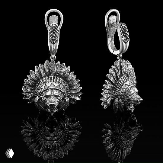 Пара серебряных подвесок с изображением стилизованных головных уборов и масок, детализированная фактура, чёрный отражающий фон, показано крупным планом.