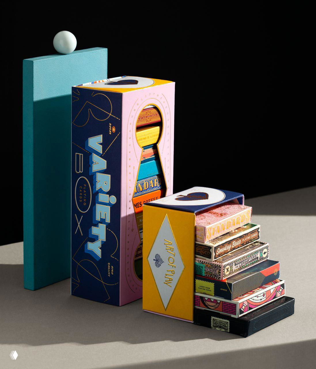 Студийная фотография набора коробок с коллекцией Art of Play: яркие коробки и стопка разноцветных колод, видна фольга и тиснение на упаковке.
