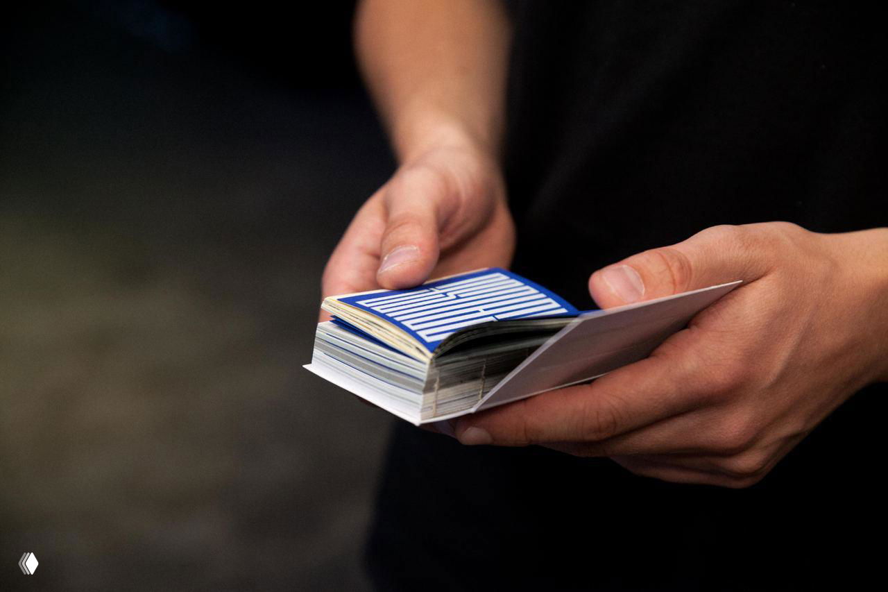 Крупные планы рук, пролистывающих маленькую книгу; контрастные шрифты и композиция разворотов хорошо видны на тёмном фоне.