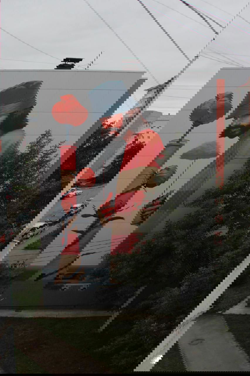 Фрагмент мурала: высокий мужчина в панаме рядом с маяком, пионы и туча, композиция символизирует ориентир и призвание на Сахалине.