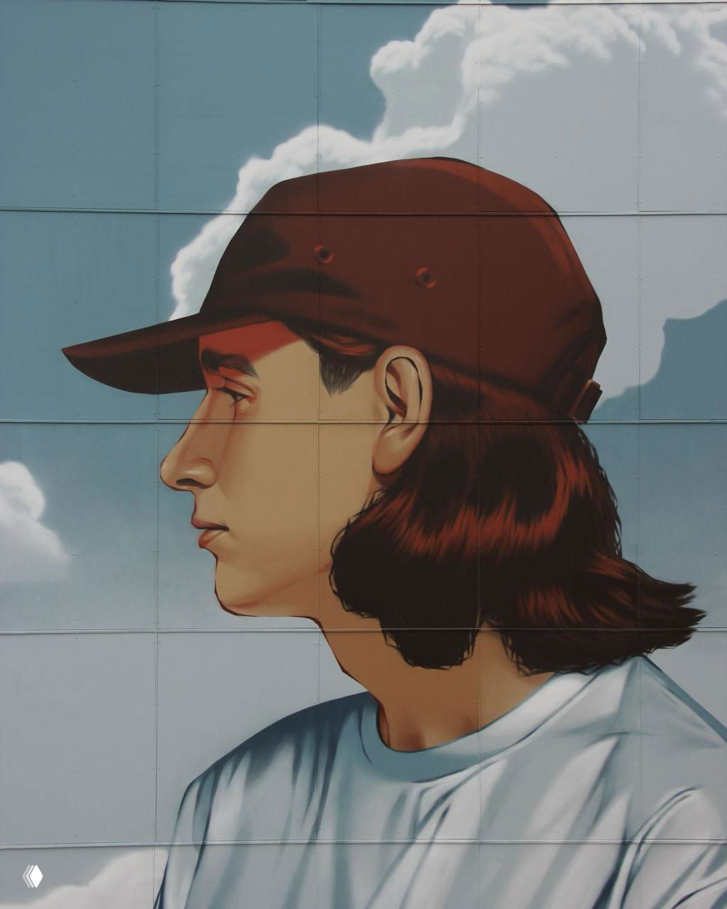 Крупный план профиля молодого мужчины в кепке на панно — детальная работа с лицом и волнистыми облаками на заднем плане фасада.