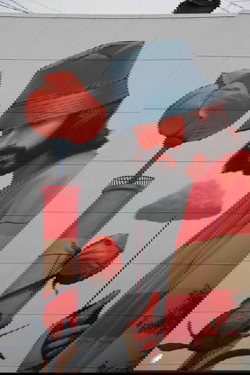 Фрагмент с маяком и цветами: красочныe пионы вверху, на фоне маяка и миниатюрного грузовика, сочетание символов и городского контекста.