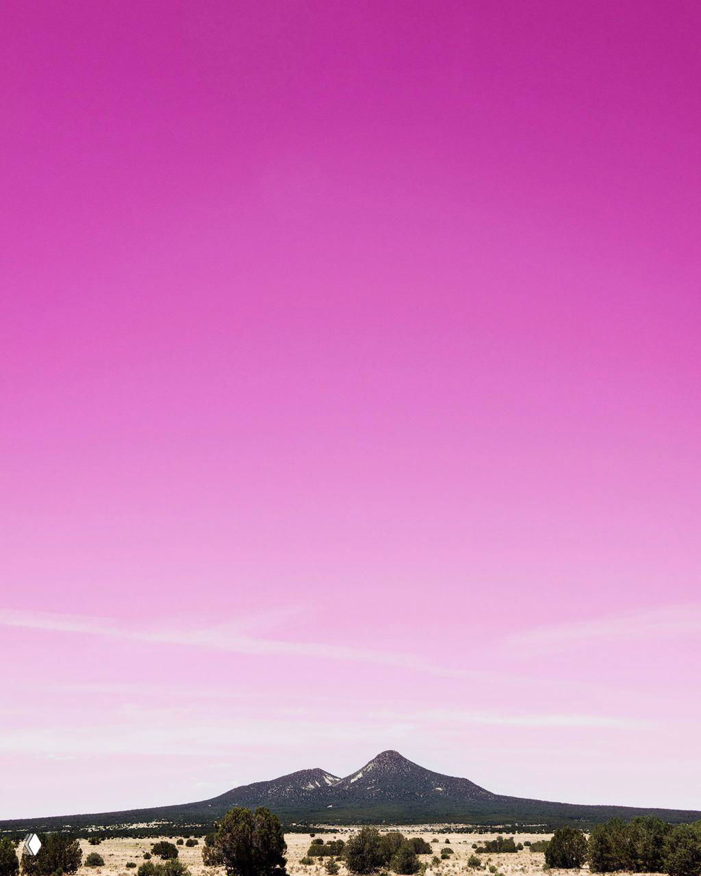 Мягкий горизонтальный градиент с вершинами гор на фоне — розово‑фиолетовое небо над ландшафтом; иллюстрация контраста природы и цвета.