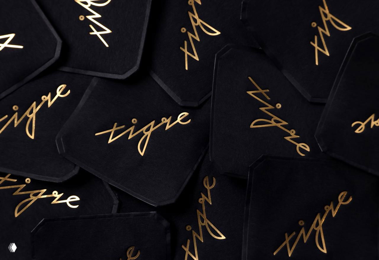 Чёрные карточки/подставки с тиснением золотым логотипом Tigre; элегантная типография и контраст матовой бумаги с фольгой.