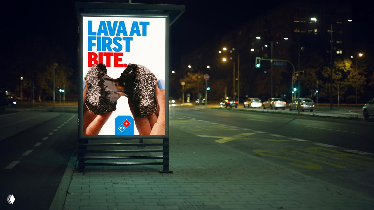 Световая уличная реклама с крупной фотографией продукта и типографикой в сине‑красной гамме, пример наружного применения айдентики Domino’s.