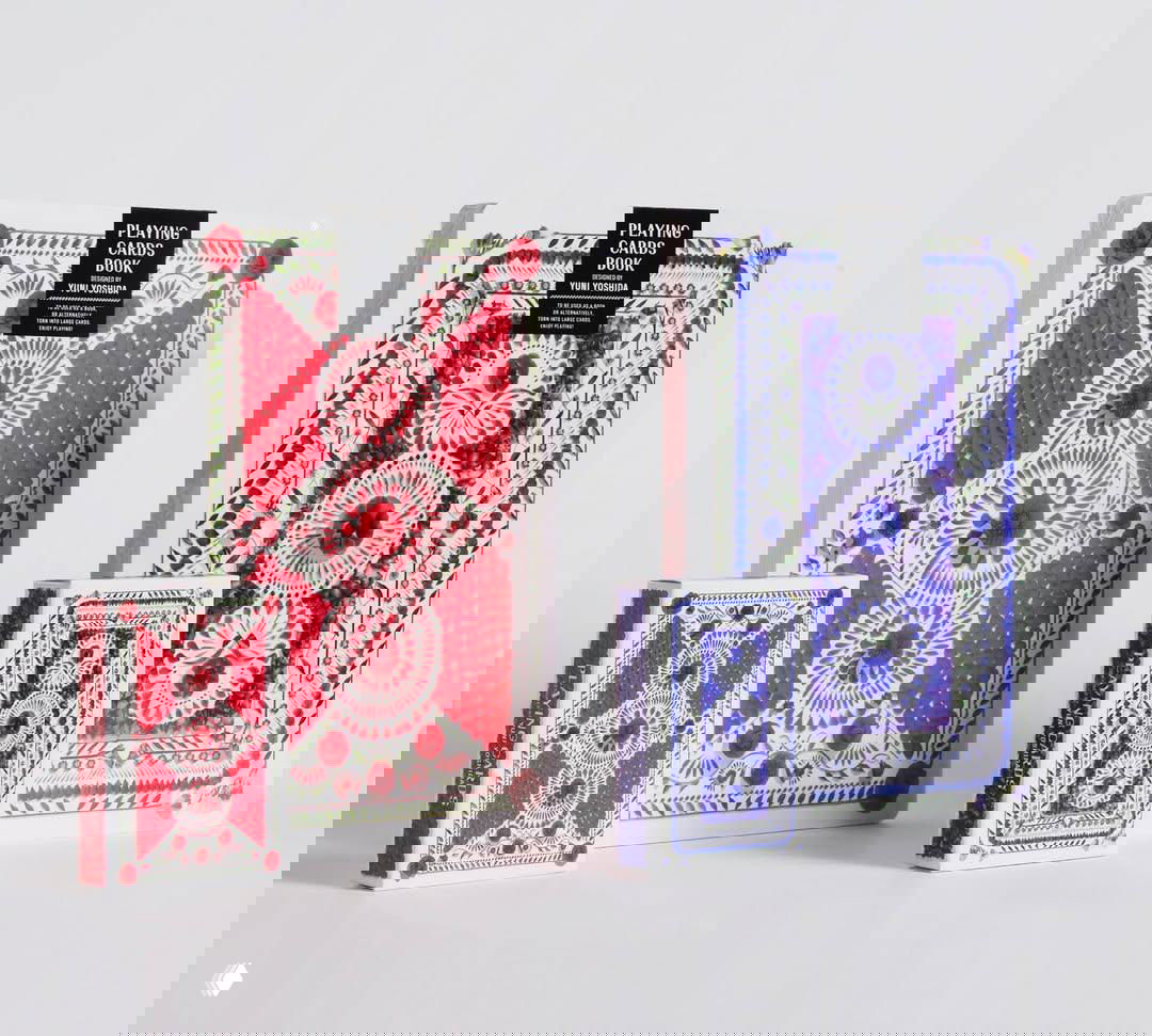 На светлом фоне две большие коробки и две маленькие колоды с орнаментальными рубашками карт в красно‑синей гамме, оформленные как натюрморт.