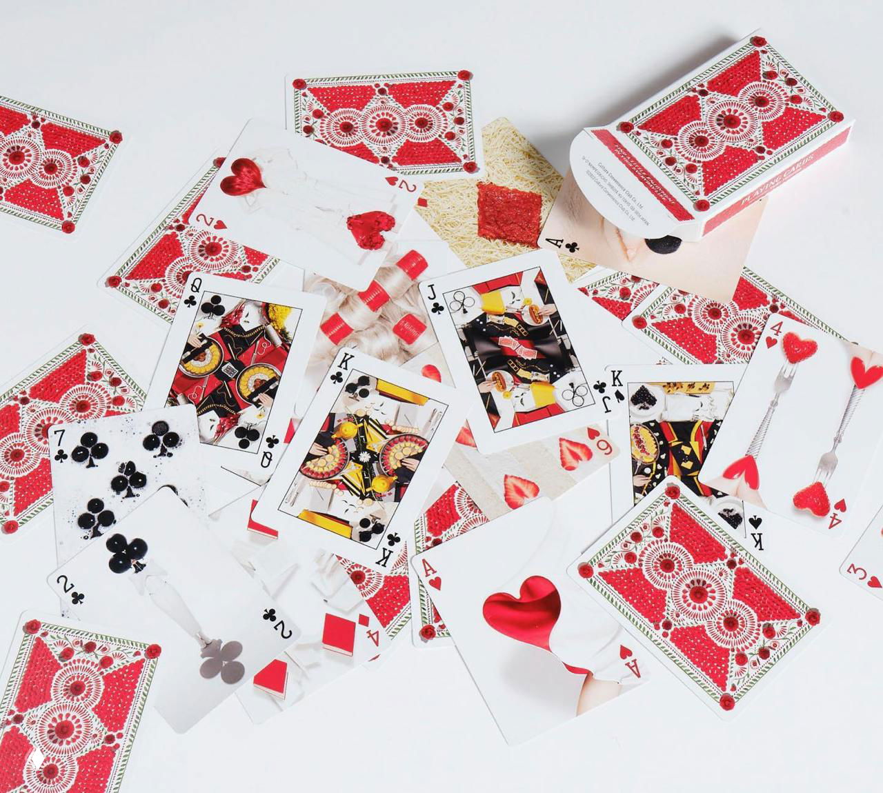 Разбросанные карты на белом столе: рубашки с красными лепестками и лицевые стороны с миниатюрными натюрмортами, фото демонстрирует детальную верстку колоды.