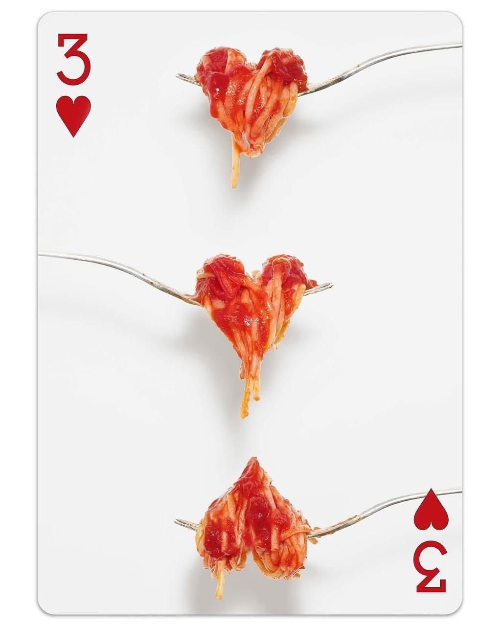 Карта с тремя сердцами из пасты на вилках на белом фоне — простые объекты превращены в узнаваемые масти и формы.