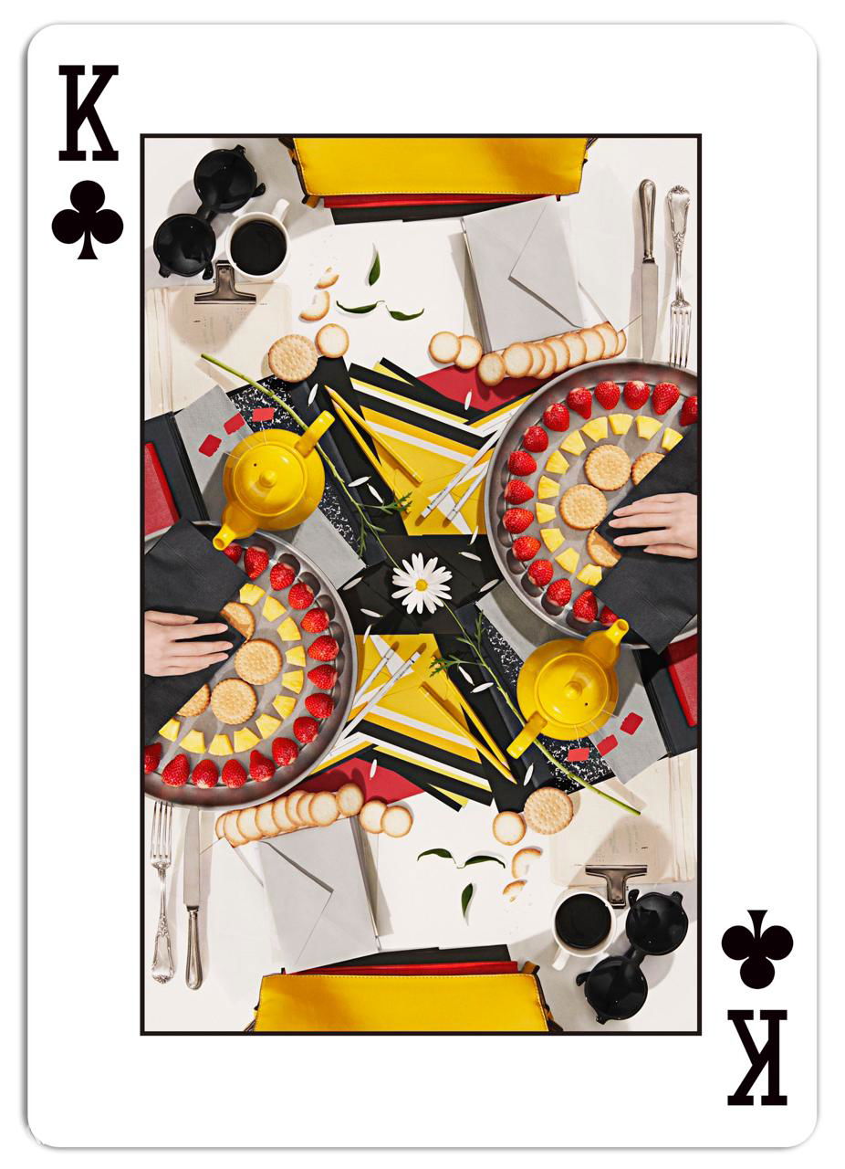 Лицевая сторона короля треф с тщательно собранной натюрмортной композицией — чайники, печенье и декоративные элементы, сложенные в зеркальную форму.