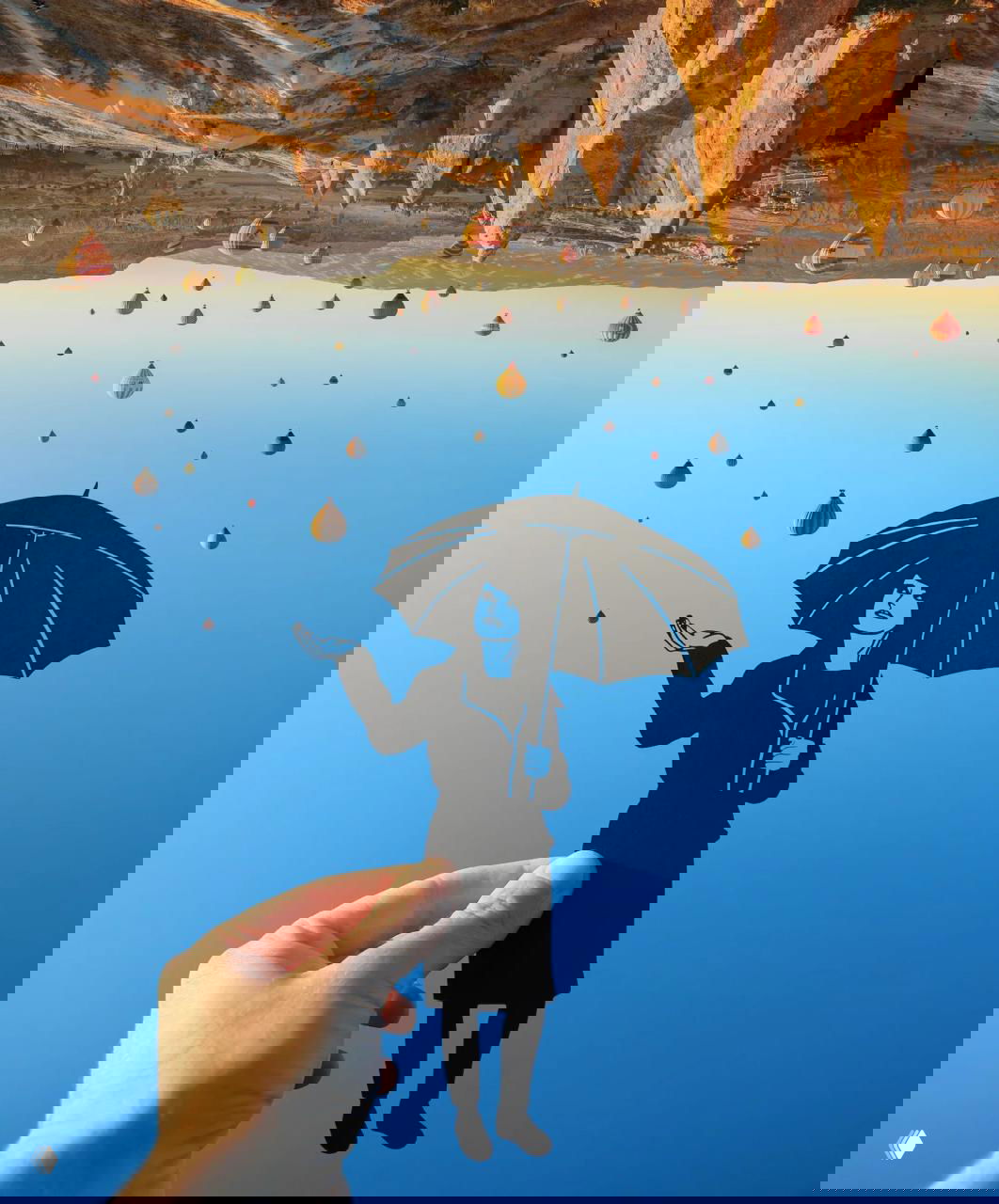 Чёрная бумажная фигура на фоне неба и горячих воздушных шаров, автор держит вырезку так, что она словно взаимодействует с пейзажем.