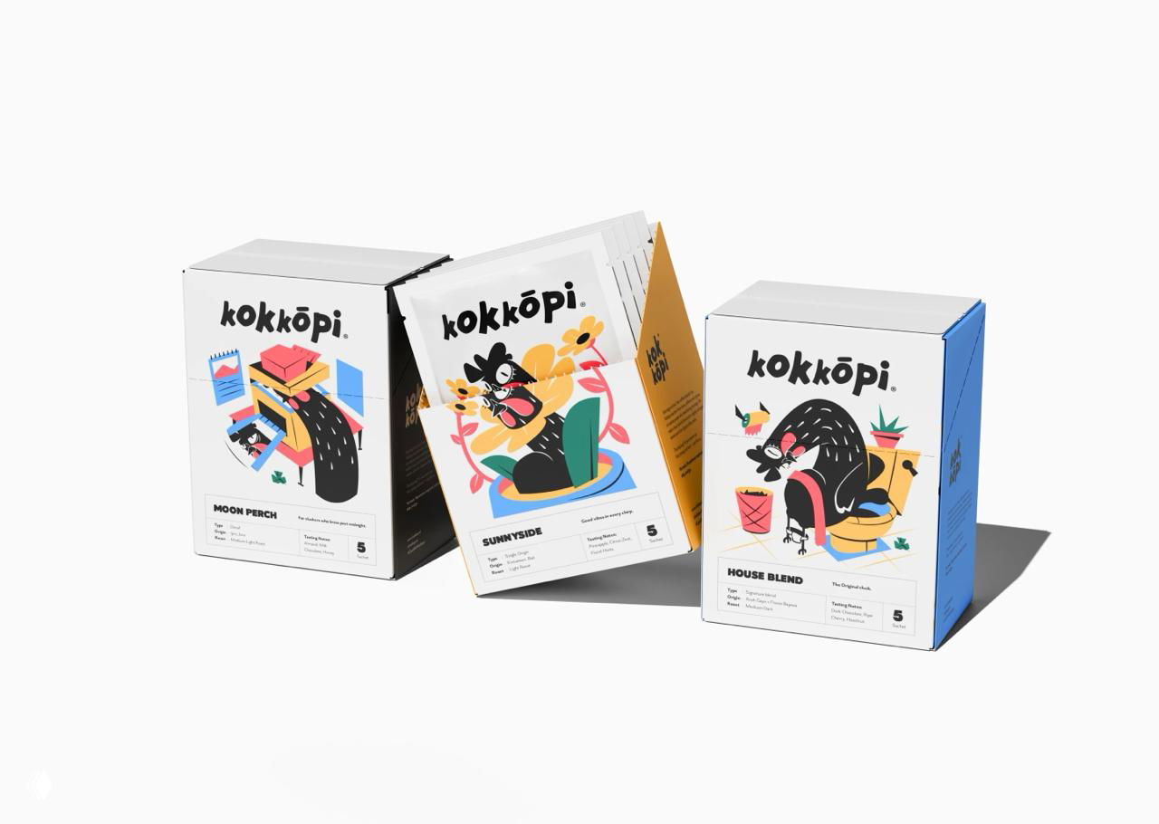 Три картонные коробки Kokkōpi с изображениями маскота и бело‑голубым цветовыми акцентом, расположенные в перспективе на светлом фоне для демонстрации дизайна.