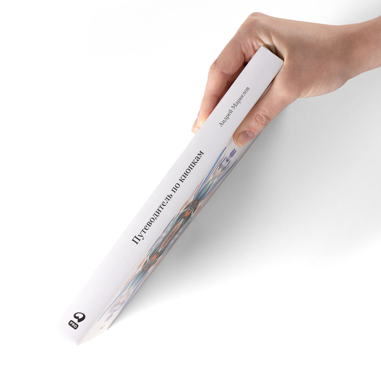 Рука держит книгу за корешок: вид сбоку на тонкую белую книгу с надписью «Путеводитель по кнопкам», человек демонстрирует формат и толщину издания.
