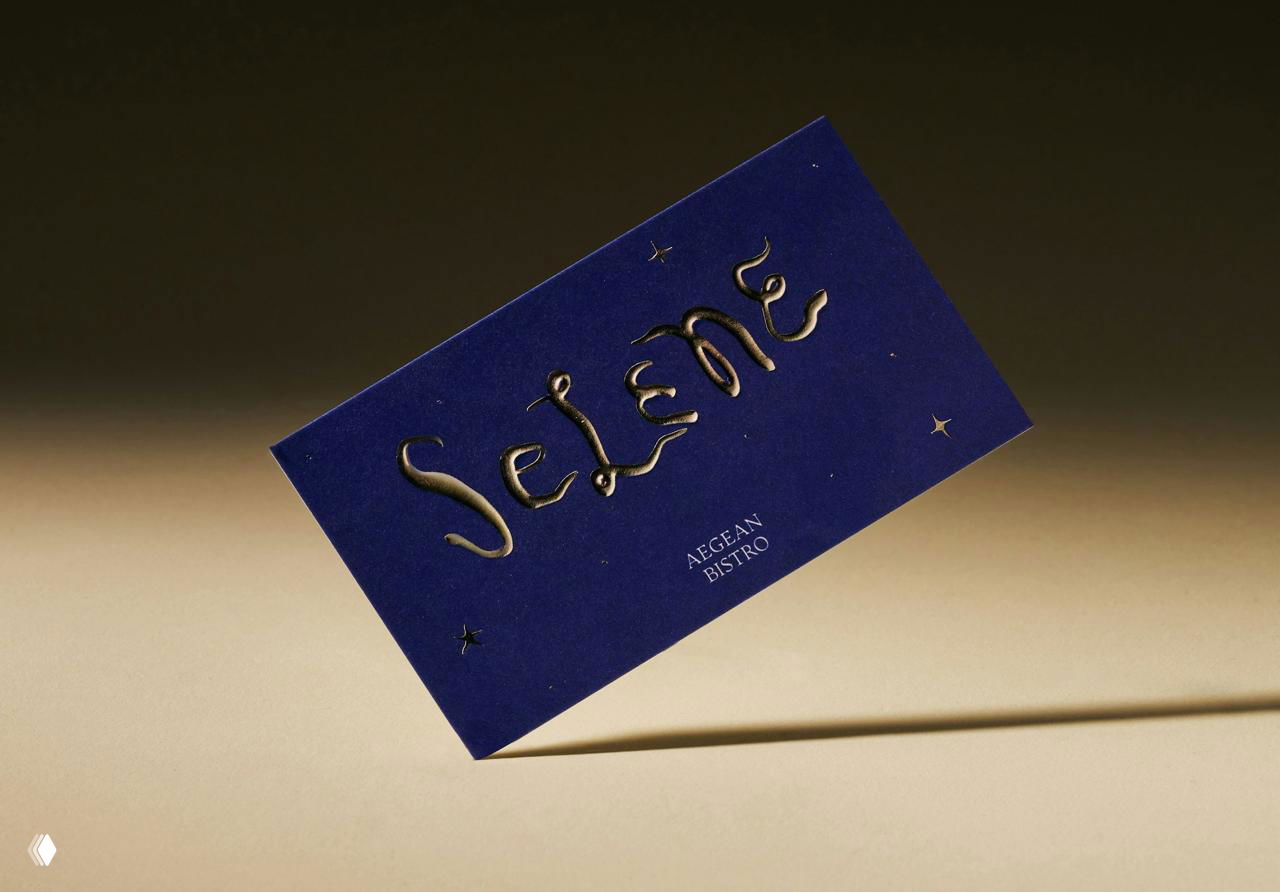 Темно‑синяя визитка Selene с золотистым тиснением логотипа на кремовом фоне, студийная подсветка и выраженная тень, премиальная айдентика.