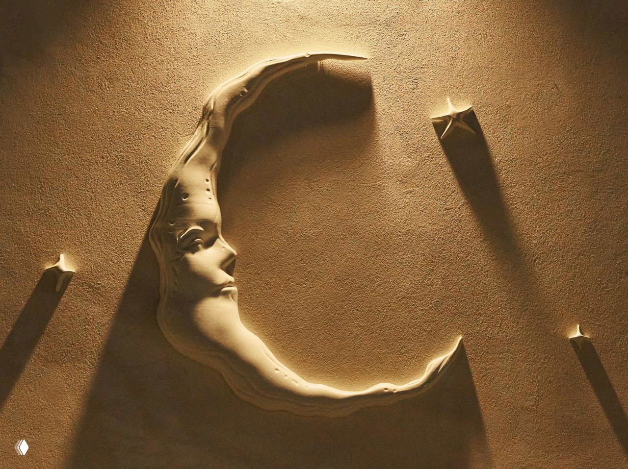 Барельеф в виде полумесяца с лицом богини Луны, выполненный в рельефе на стене; тёплая студийная подсветка подчёркивает текстуру и тени.