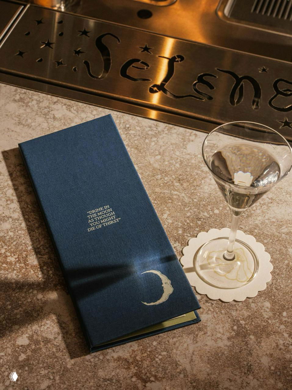 Темно‑синее меню Selene с тиснёным полумесяцем рядом с бокалом; сценическая студийная композиция подчёркивает печать и текстуру переплёта.