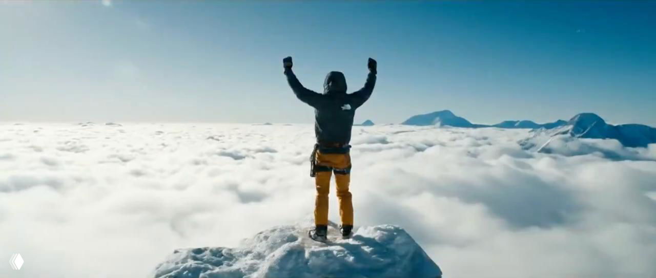 Эпический кинематографический кадр: альпинист стоит на вершине над морем облаков с поднятыми руками, широкая панорама как пример промта для вдохновляющего ролика.
