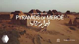 Панорамный вид на ряд нубийских пирамид Мероэ в пустынном ландшафте Судана, видны руины и песчаная равнина, рекламная надпись проекта в кадре