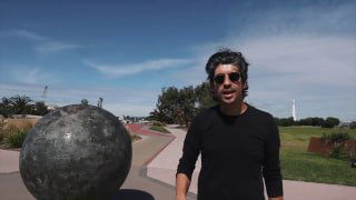 Металлическая модель планеты на береговой набережной Мельбурна; на заднем плане прогулочная аллея, зелень и человек рядом.