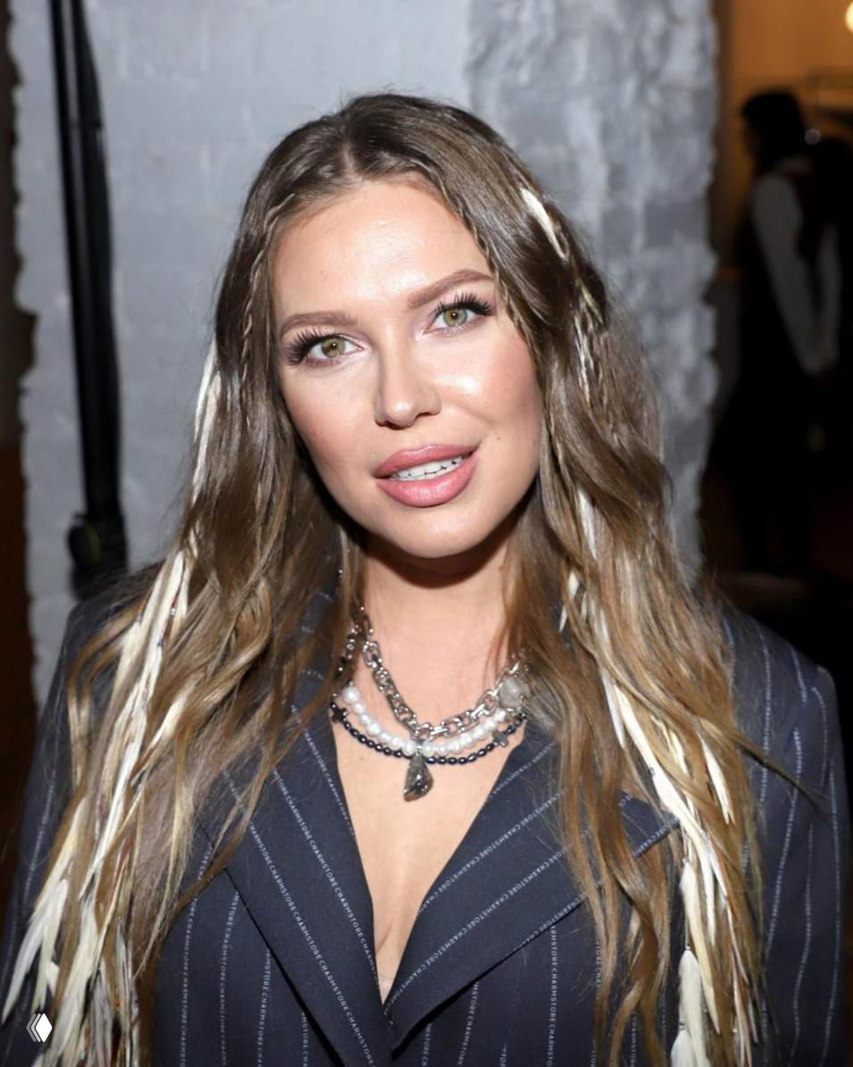 Крупный портрет женщины в светском образе — лицо и плечи в помещении, мягкое освещение, акцент на макияже и украшениях; фото сделано на мероприятии.