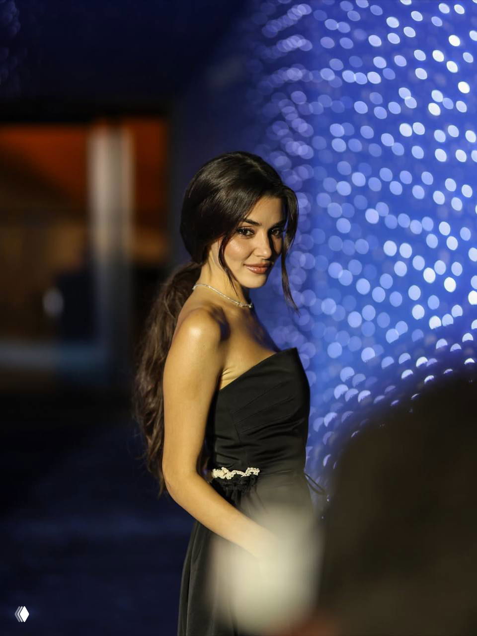 Ханде Эрчел в чёрном платье снята в анфас на фоне размытых синих огней — кадр с премьерного показа фильма «Два мира, одно желание»