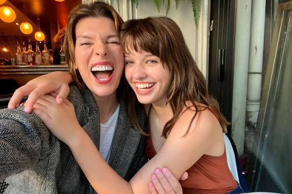 Улыбающаяся женщина и подросток обнимаются в уютном интерьере кафе; тёплый, искренний кадр крупным планом, дружеская атмосфера.