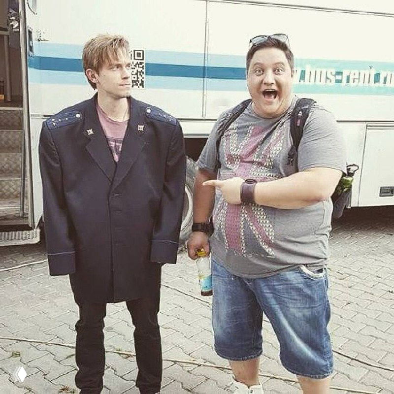 Деформированное чёрно‑белое фото: трое мужчин на улице, один закрывает лицо рукой — символическая иллюстрация к прощанию актёра и дружеской памяти.